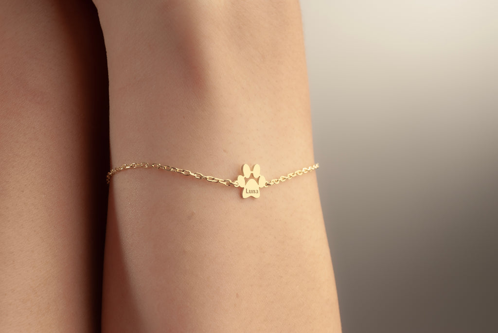 Gold dog paw name bracelet worn on a woman’s wrist