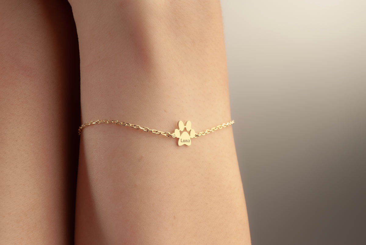 Gold dog paw name bracelet worn on a woman’s wrist